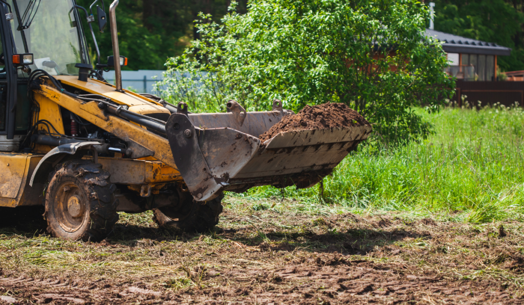 Yellow wheeled loader moving dark organic soil during site scalping and surface preparation on a residential construction site in Bradenton Florida
