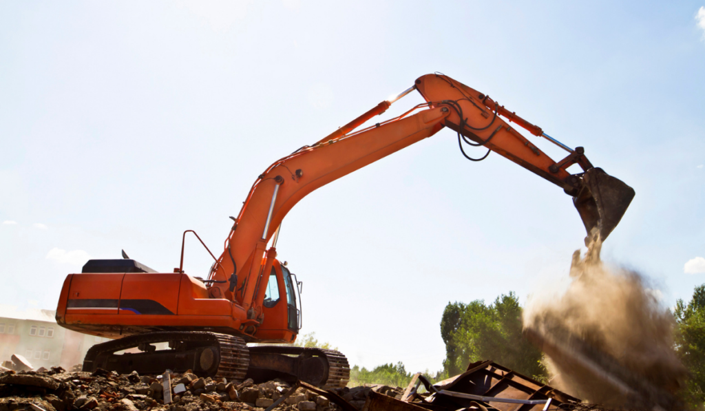 Large orange excavator working commercial demolition site in Bradenton FL clearing structural debris and concrete rubble under clear blue sky